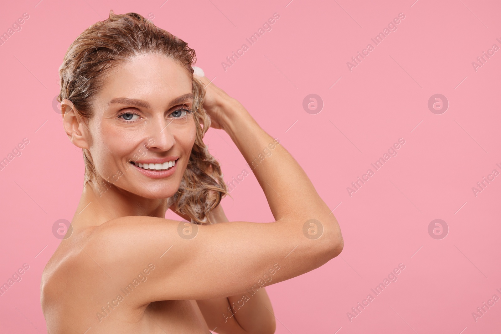 Photo of Beautiful happy woman washing hair on pink background. Space for text