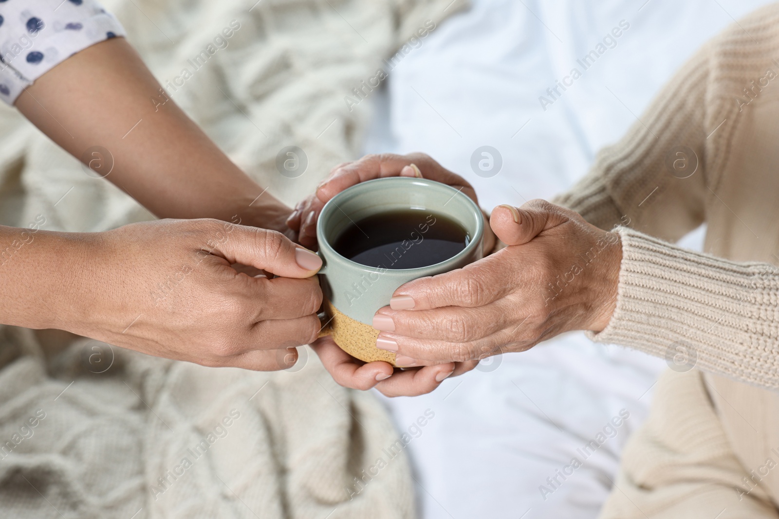 Photo of Caregiver giving drink to elderly woman at home, closeup