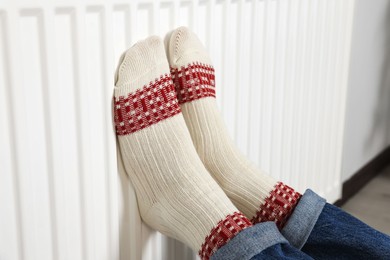 Photo of Woman warming legs on heating radiator near white wall, closeup