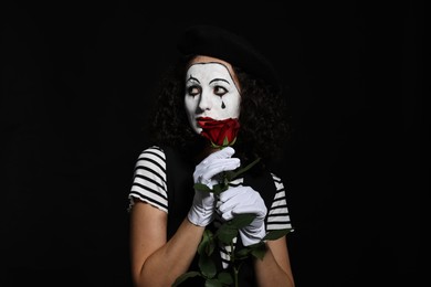 Photo of Young woman in mime costume with red rose posing on black background