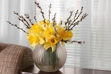 Photo of Bouquet of beautiful yellow daffodils and willow twigs in vase on table