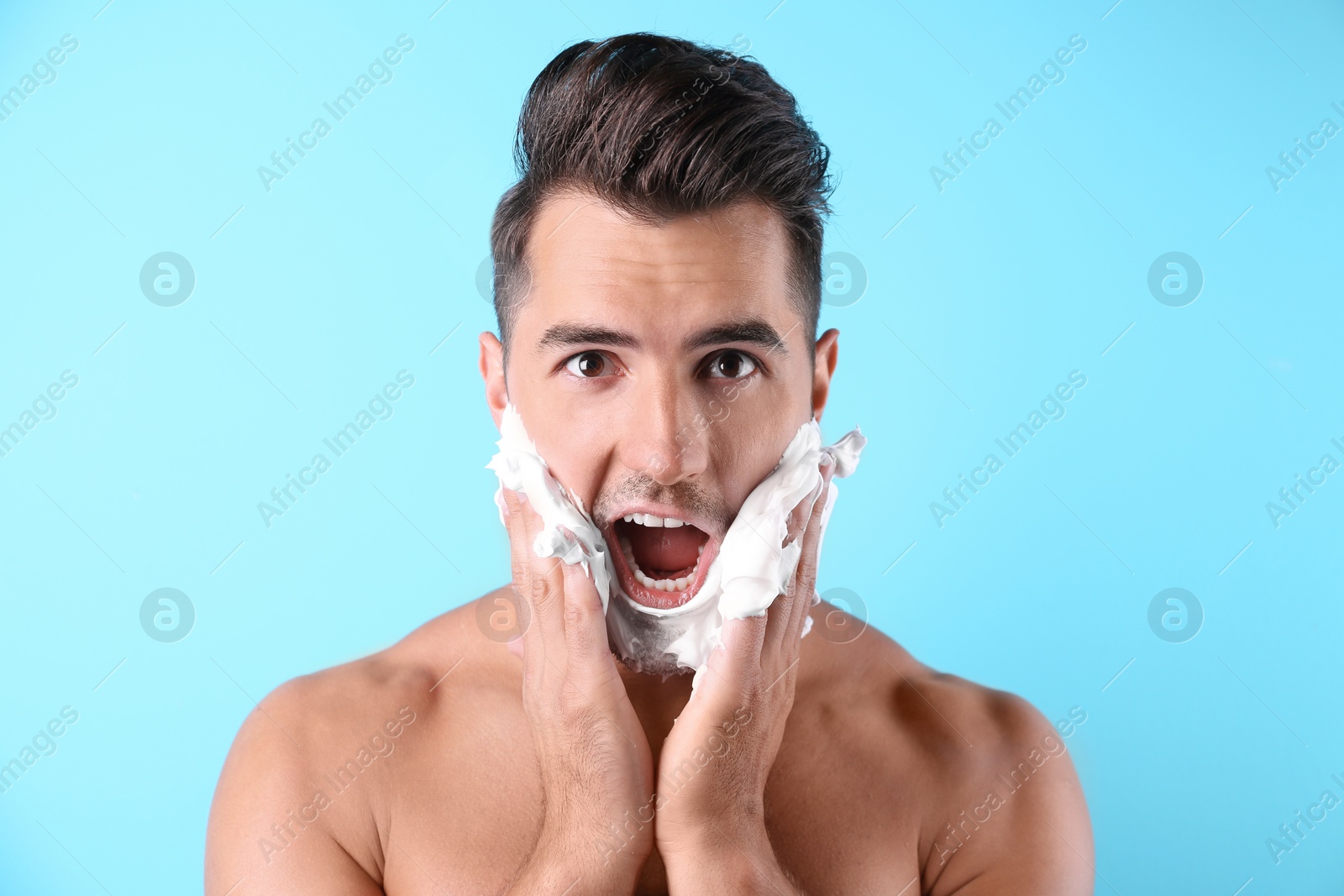 Photo of Handsome young man applying shaving foam on color background