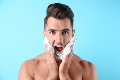 Handsome young man applying shaving foam on color background