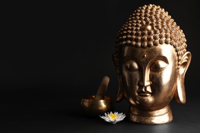 Photo of Beautiful golden Buddha sculpture with singing bowl and flower on black background. Space for text