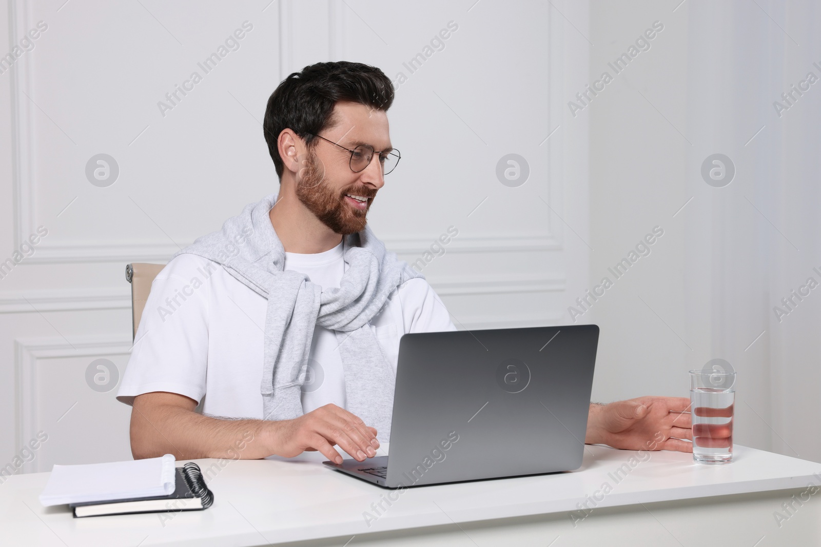 Photo of Man with laptop and glass of water at white table indoors