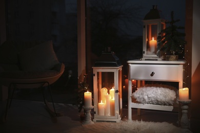 Beautiful lanterns with burning candles and Christmas decor in room. Interior design