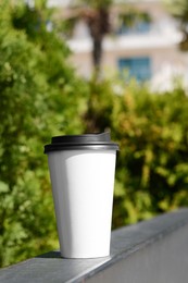 Photo of Takeaway coffee cup on metal railing outdoors. Space for text