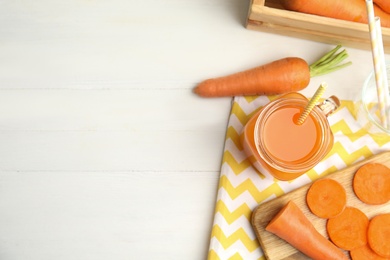 Photo of Freshly made carrot juice in mason jar on white table, flat lay. Space for text