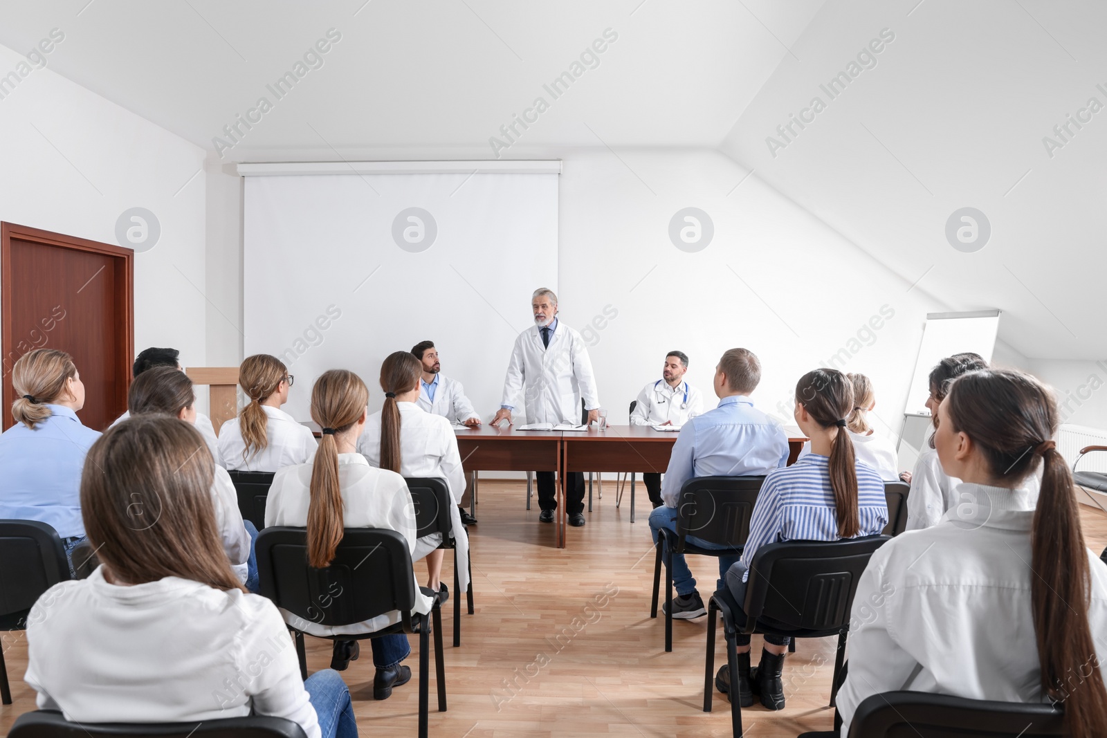 Photo of Senior doctor giving lecture near projection screen in conference room