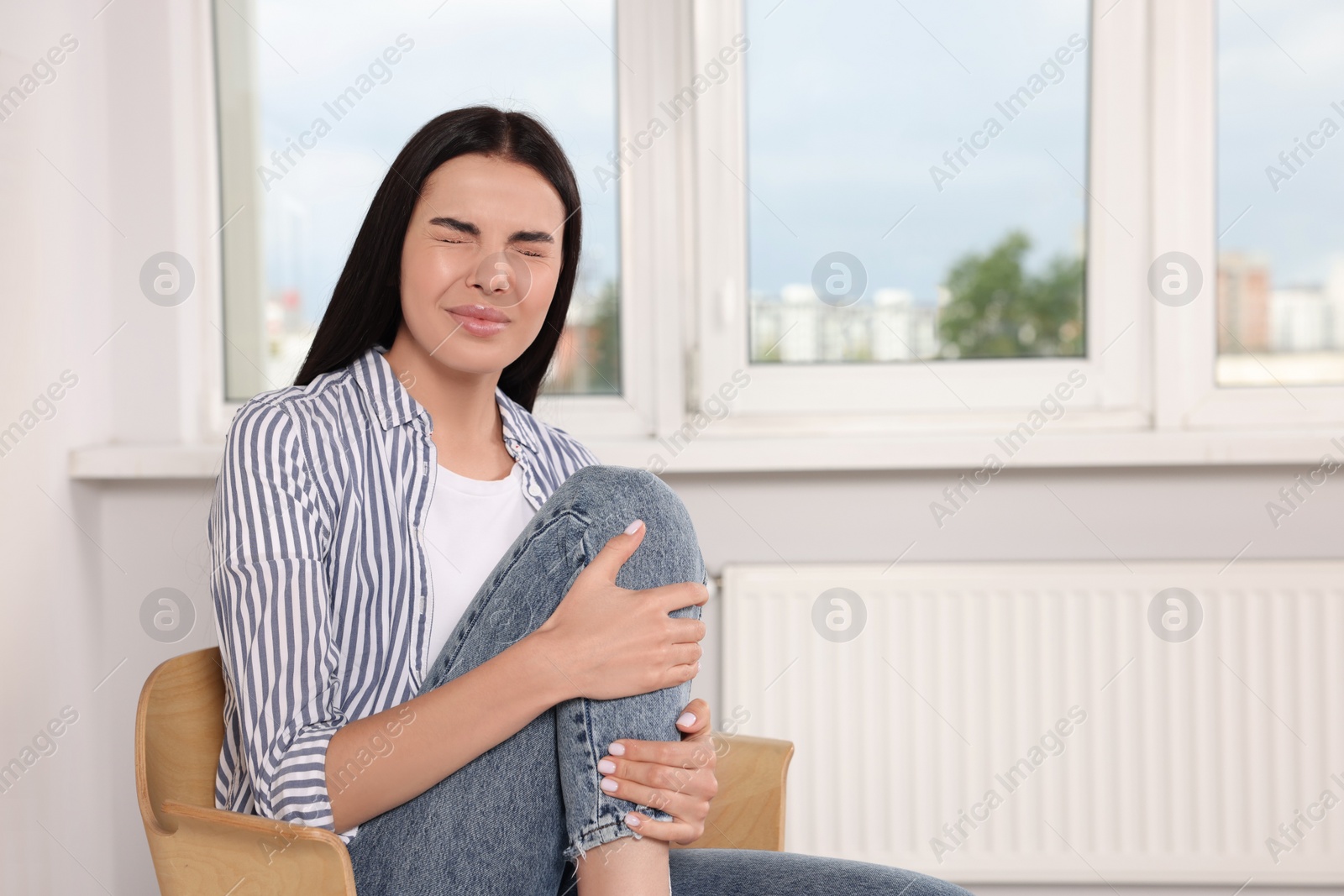 Photo of Woman suffering from leg pain on chair at home, space for text