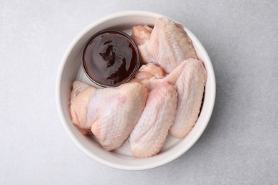 Plate with marinade and raw chicken wings on light textured table, top view