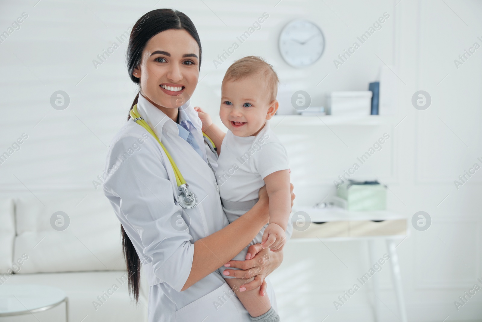 Photo of Young pediatrician with cute little baby in clinic. Space for text