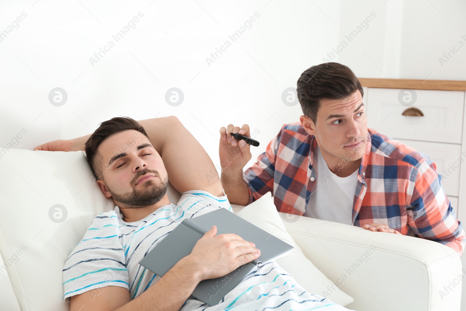 Photo of Man with marker near sleeping friend indoors. April fool's day