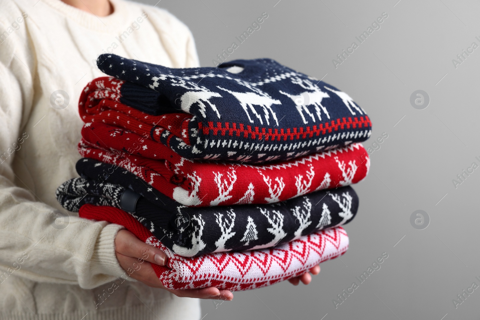 Photo of Woman holding stack of different Christmas sweaters on grey background, closeup