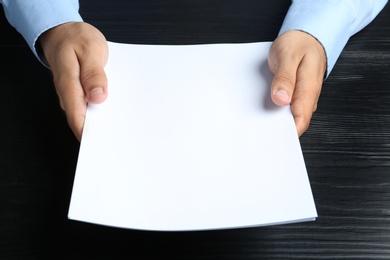 Man holding blank paper sheets for brochure at black wooden table. Mock up