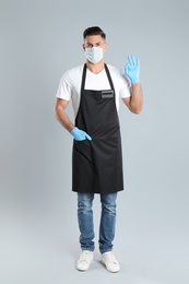 Photo of Waiter wearing medical face mask on light grey background