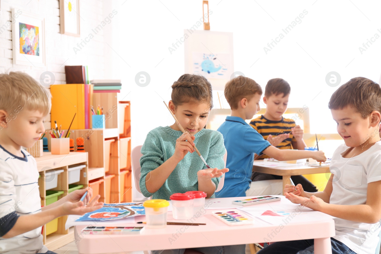 Photo of Cute little children painting their palms at table in room