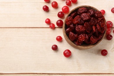 Photo of Dried cranberries in bowl and fresh berries on wooden table, top view. Space for text