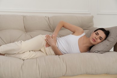 Woman suffering from appendicitis inflammation on sofa indoors