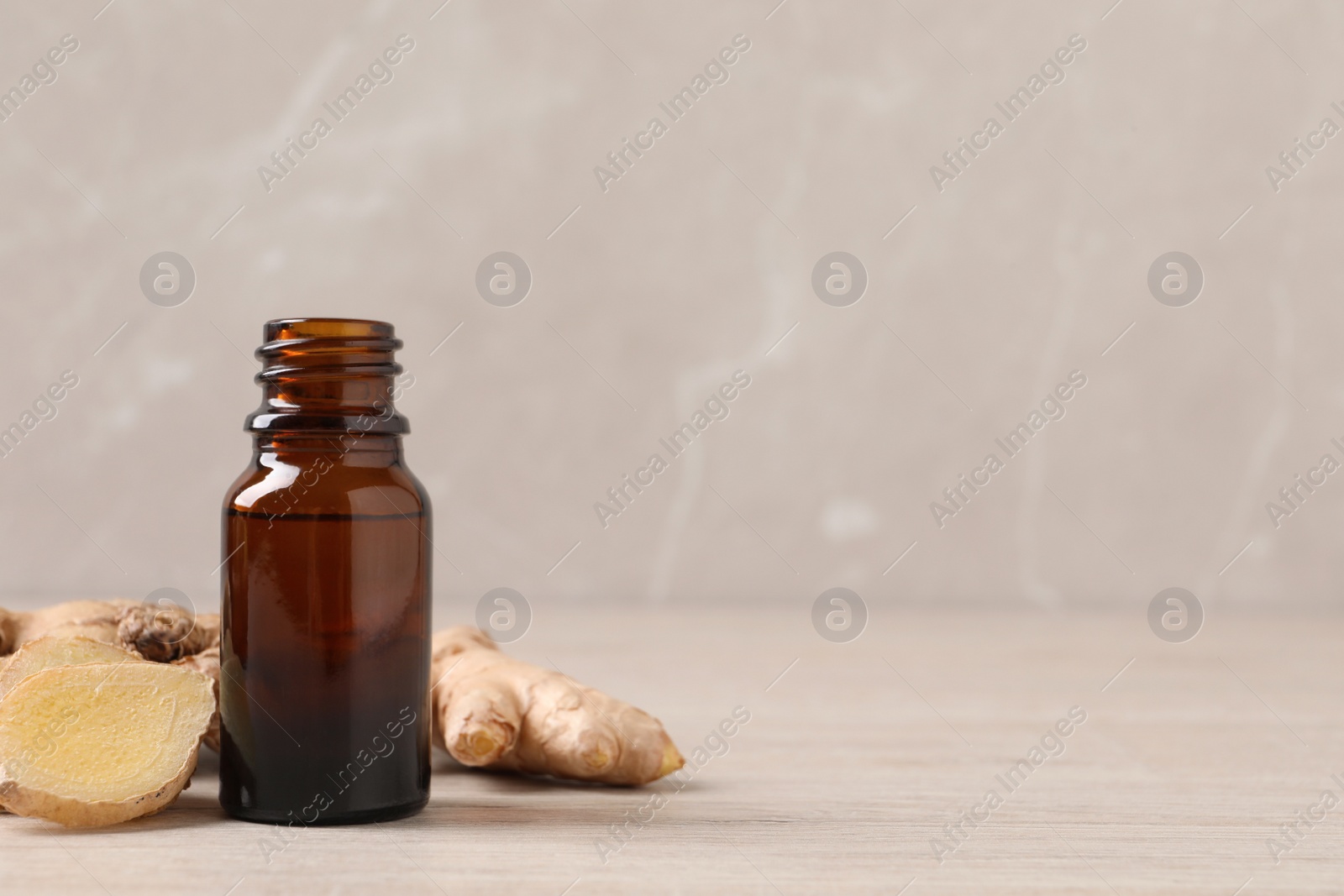 Photo of Glass bottle of essential oil and ginger root on beige wooden table, space for text