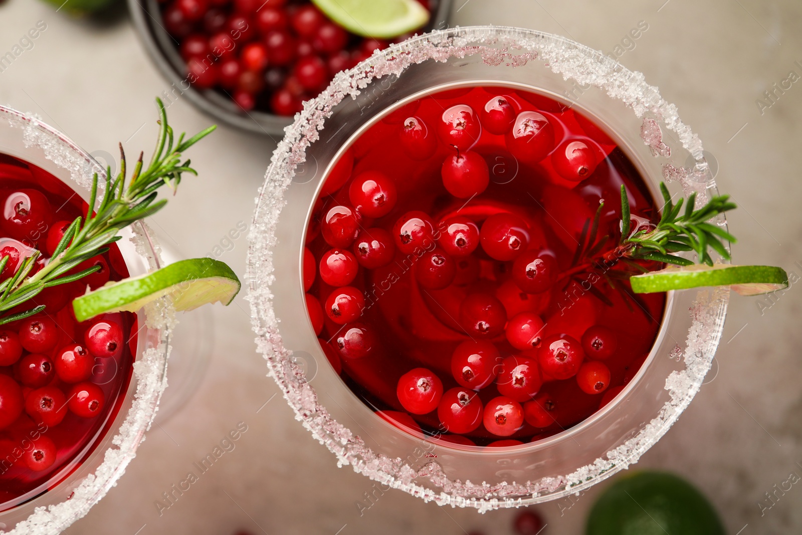 Photo of Tasty cranberry cocktail with rosemary and lime in glasses on grey table, flat lay