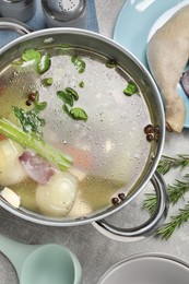 Pot with tasty bouillon and different ingredients on light grey table, flat lay