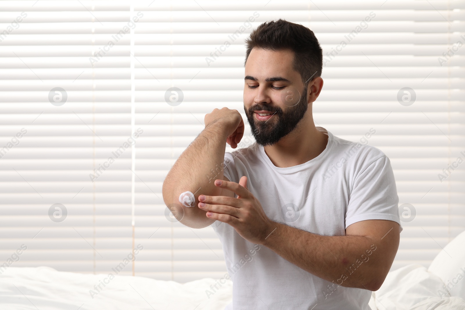 Photo of Man with dry skin applying cream onto his elbow indoors, space for text