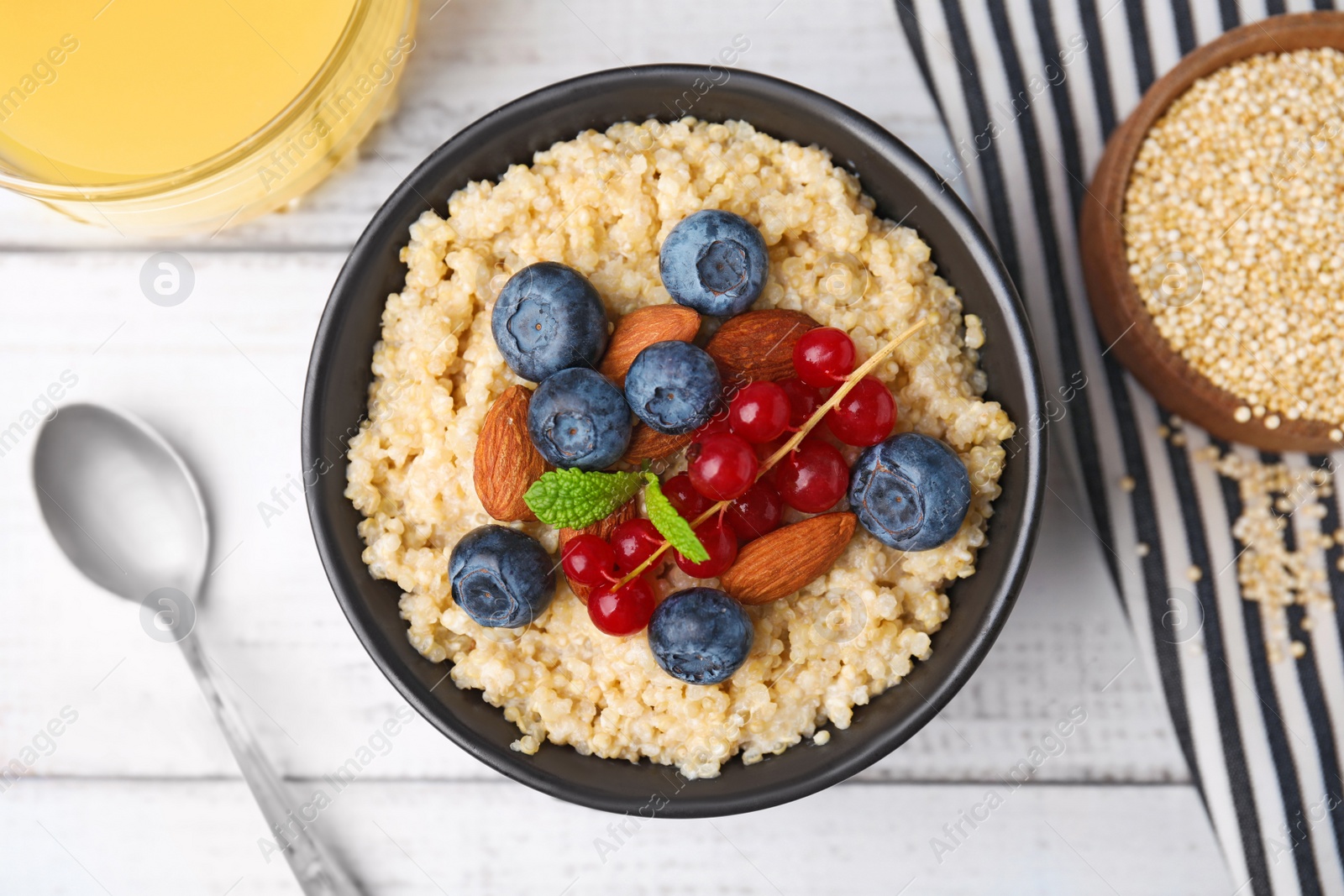 Photo of Bowl of delicious cooked quinoa with almonds, cranberries and blueberries on white wooden table, flat lay