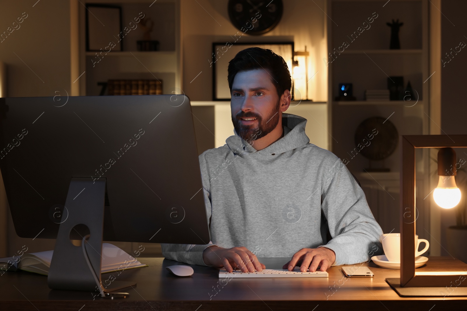 Photo of Home workplace. Man working with computer at wooden desk in room at night