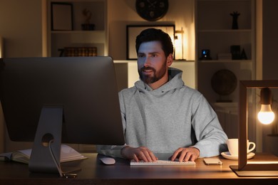 Photo of Home workplace. Man working with computer at wooden desk in room at night