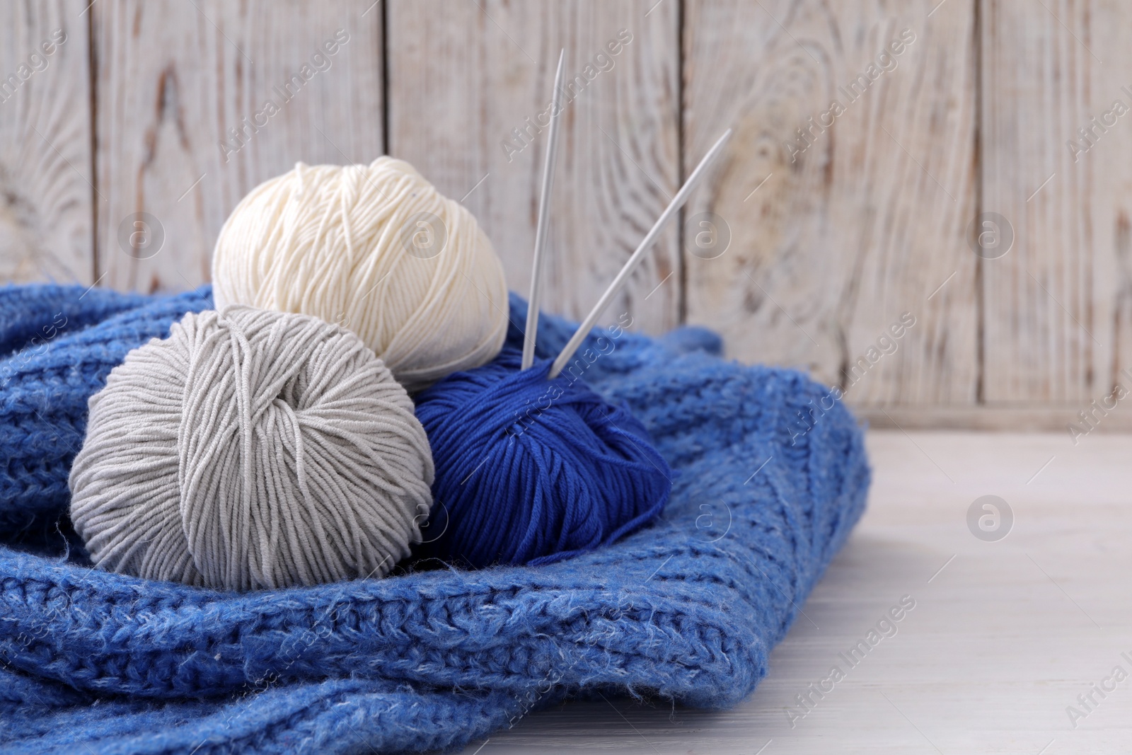 Photo of Soft woolen yarns with knitting needles and sweater on white table, closeup. Space for text