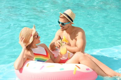 Photo of Young couple with cocktails in pool on sunny day