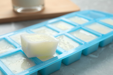 Ice cube tray with frozen milk on grey table, closeup