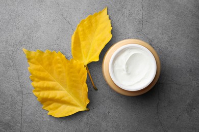 Jar of face cream and yellow leaves on grey table, top view