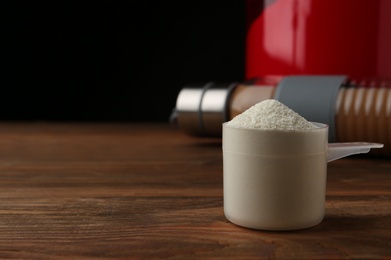 Photo of Measuring scoop of protein powder on wooden table. Space for text