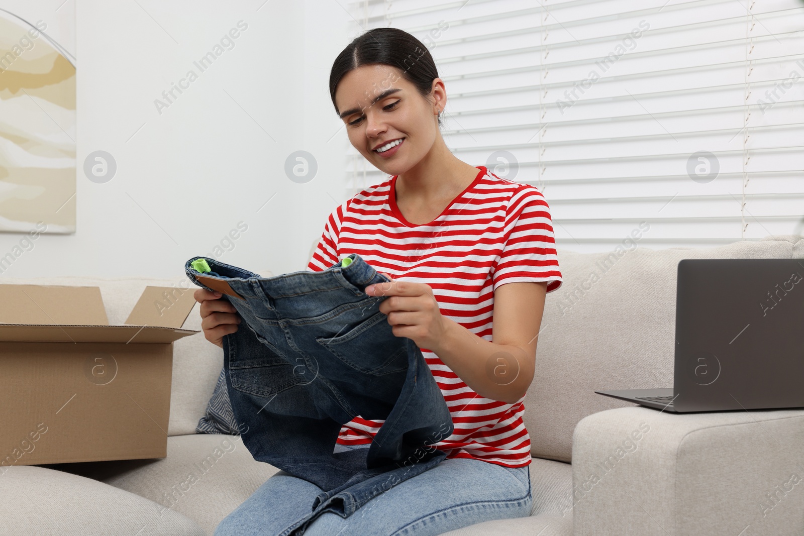 Photo of Young woman with just unpacked new jeans at home. Online shopping