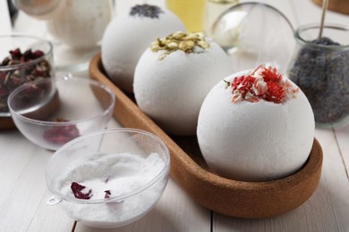 Photo of Different bath bombs and ingredients on white wooden table, closeup