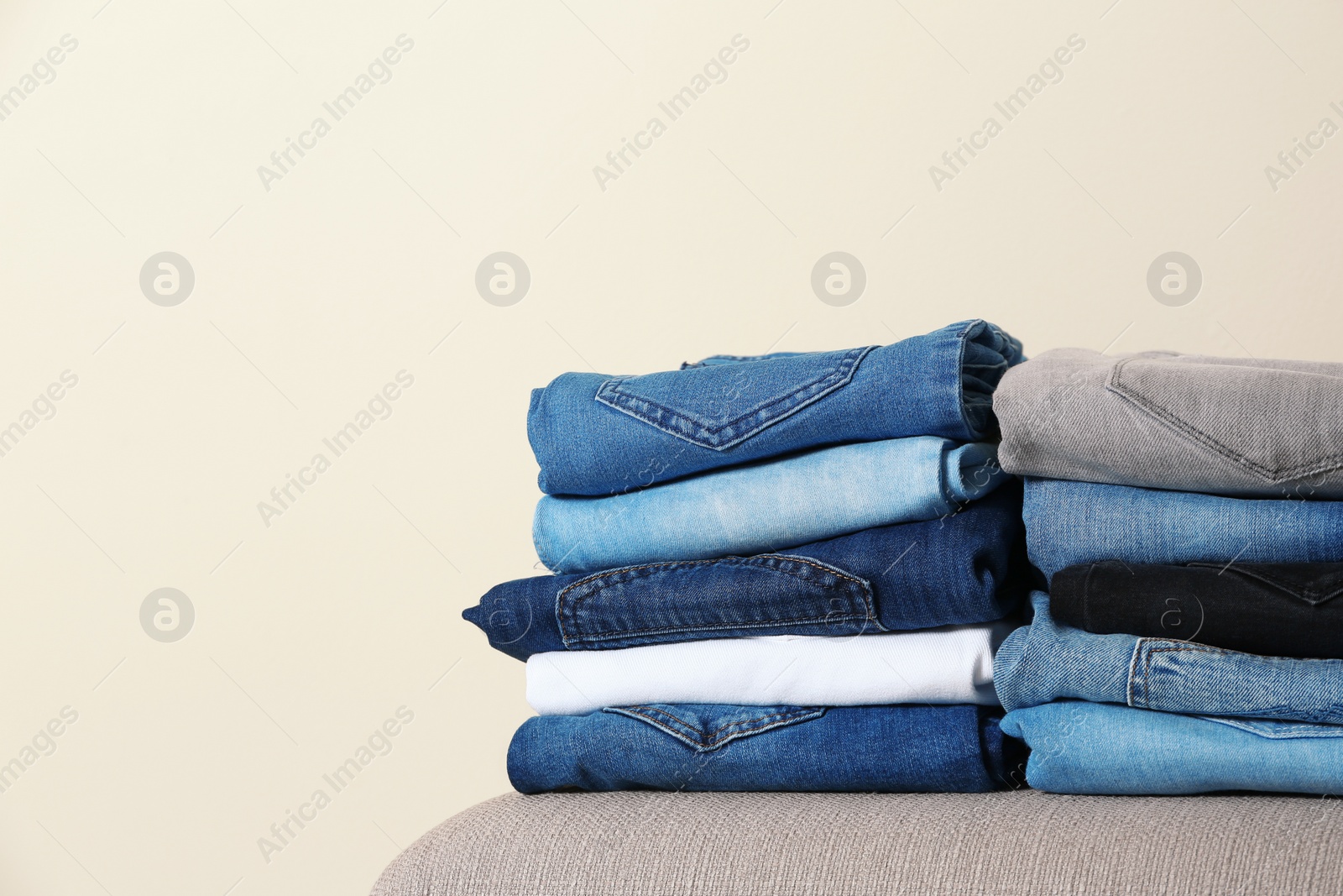 Photo of Stack of different jeans on ottoman against light background. Space for text