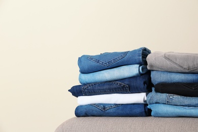 Photo of Stack of different jeans on ottoman against light background. Space for text