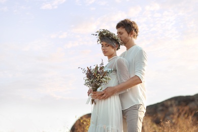 Happy newlyweds with beautiful field bouquet outdoors