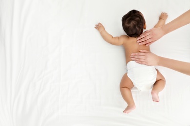 Photo of Top view of mother and her cute child on white bed, space for text. Baby massage and exercises