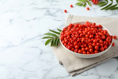 Photo of Fresh ripe rowan berries in bowl on white marble table, space for text