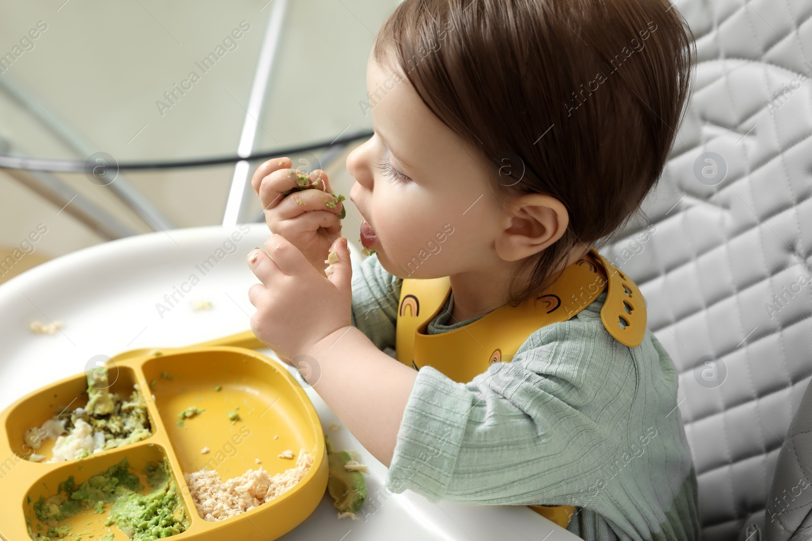 Photo of Cute little baby eating healthy food in high chair indoors