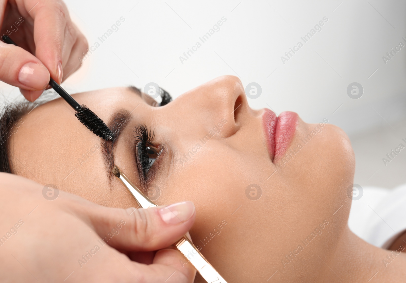 Photo of Young woman having professional eyebrow correction procedure in beauty salon