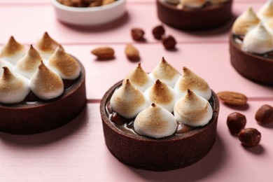 Photo of Delicious salted caramel chocolate meringue tarts and nuts on pink wooden table, closeup