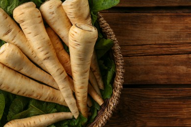 Photo of Fresh ripe parsnips in wicker basket on wooden table, top view. Space for text