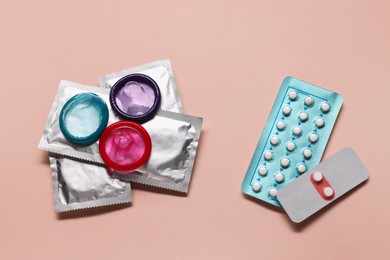Photo of Birth control pills and condoms on pink background, flat lay. Choosing method of contraception