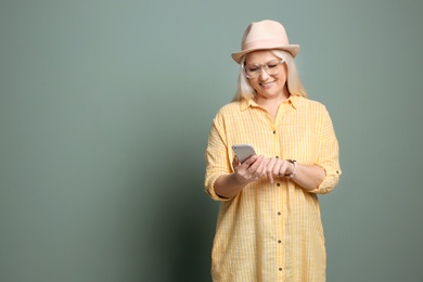 Mature woman using mobile phone on color background