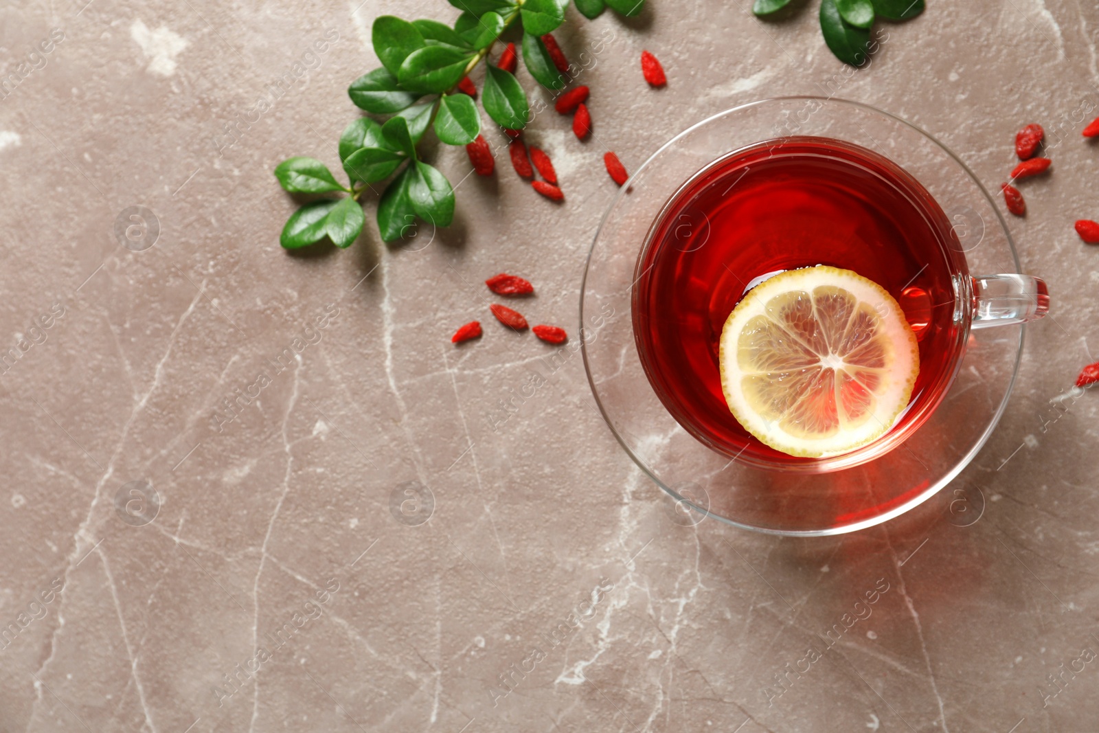 Photo of Glass cup of healthy goji tea with lemon on beige marble table, flat lay. Space for text