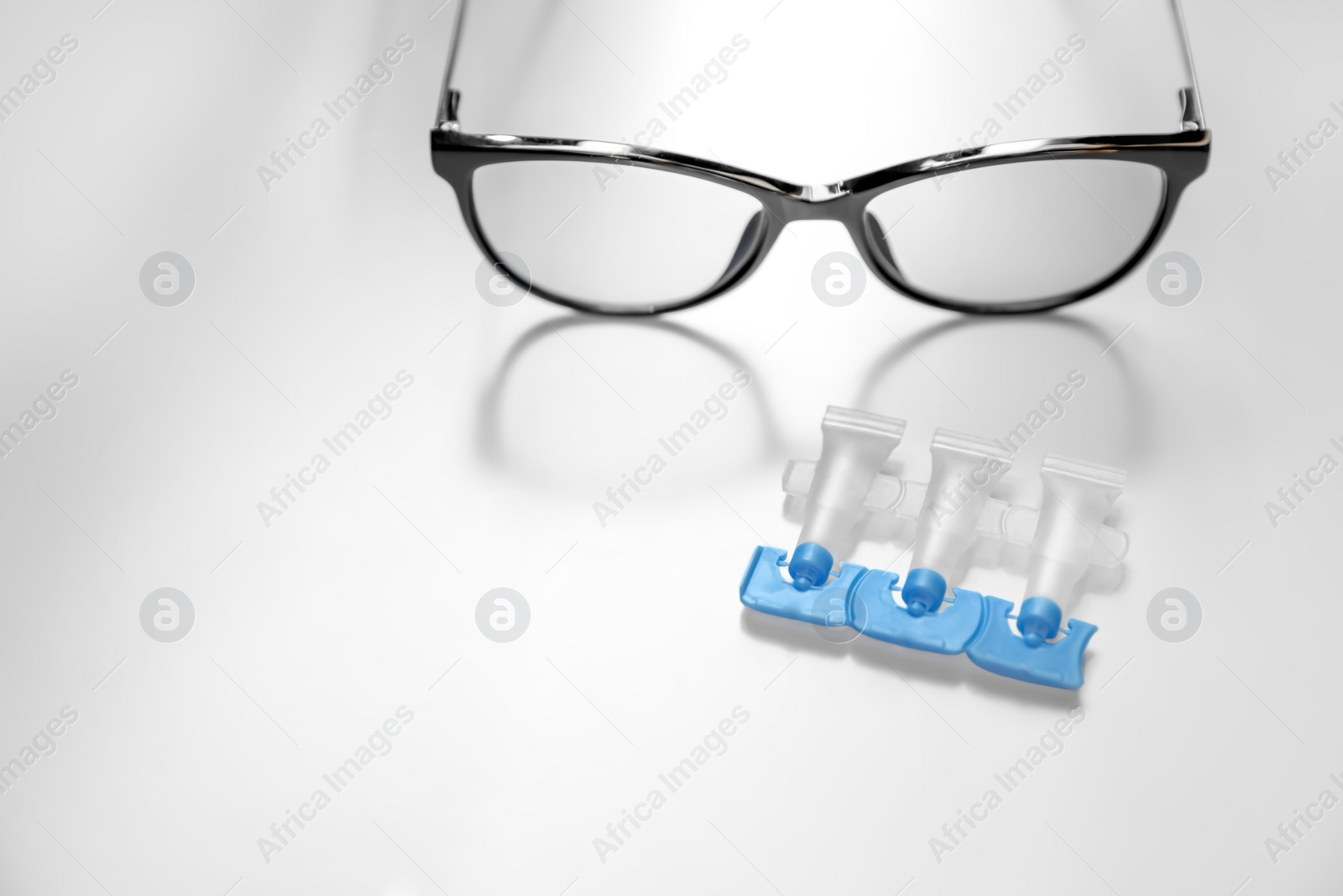 Photo of Single dose eye drops and glasses on white table, space for text